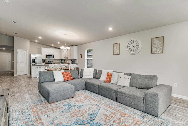 living room featuring light hardwood / wood-style flooring, lofted ceiling, and a notable chandelier