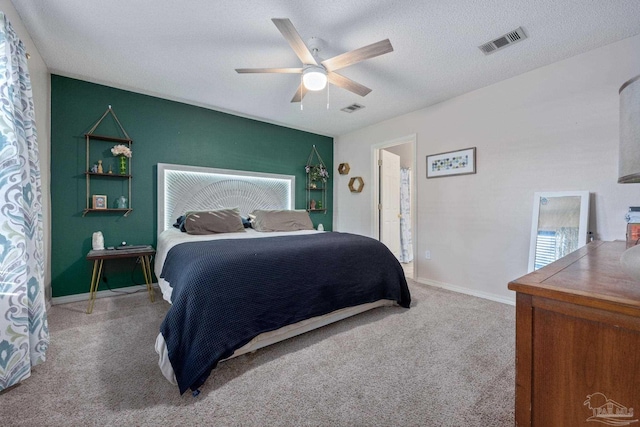 bedroom featuring ceiling fan, connected bathroom, light colored carpet, and a textured ceiling