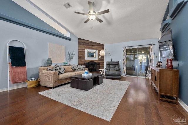 living room featuring a textured ceiling, lofted ceiling, a large fireplace, dark hardwood / wood-style floors, and ceiling fan