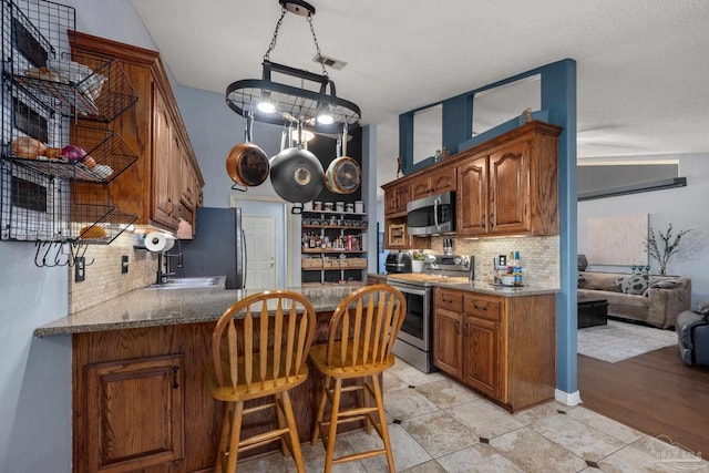 kitchen with kitchen peninsula, appliances with stainless steel finishes, decorative light fixtures, sink, and tasteful backsplash