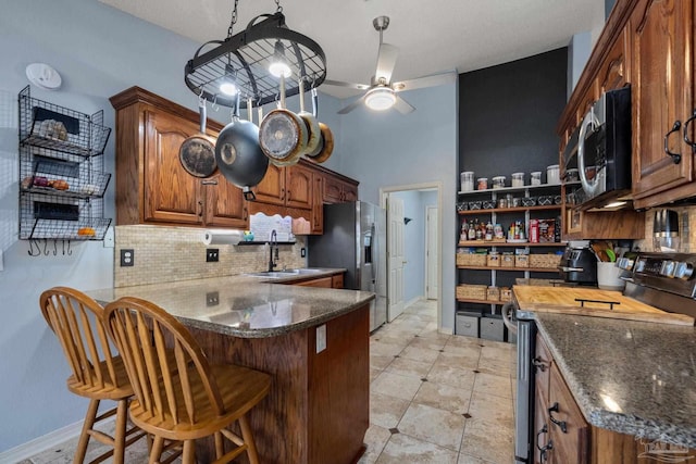 kitchen with kitchen peninsula, appliances with stainless steel finishes, sink, backsplash, and a breakfast bar