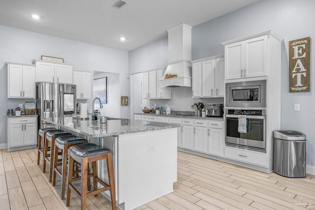 kitchen with stainless steel appliances, white cabinetry, a center island with sink, and a kitchen bar