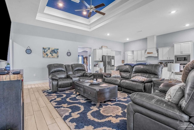 living room with a raised ceiling, crown molding, and ceiling fan