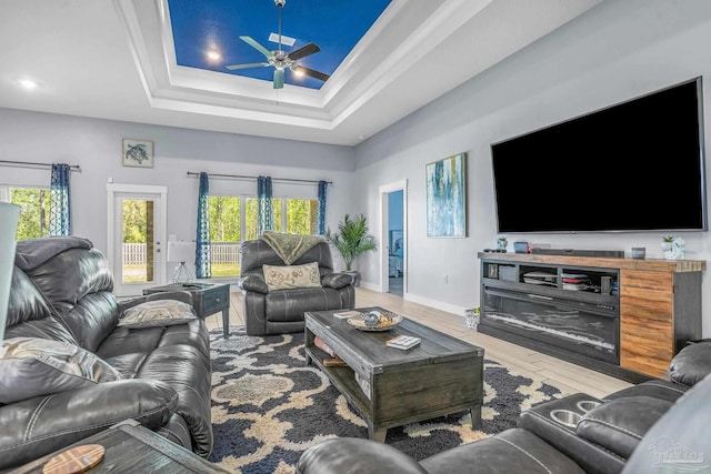 living room featuring ceiling fan, plenty of natural light, a tray ceiling, and wood-type flooring