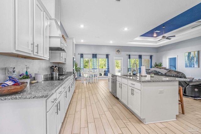 kitchen with a breakfast bar, dishwasher, light stone countertops, an island with sink, and white cabinets