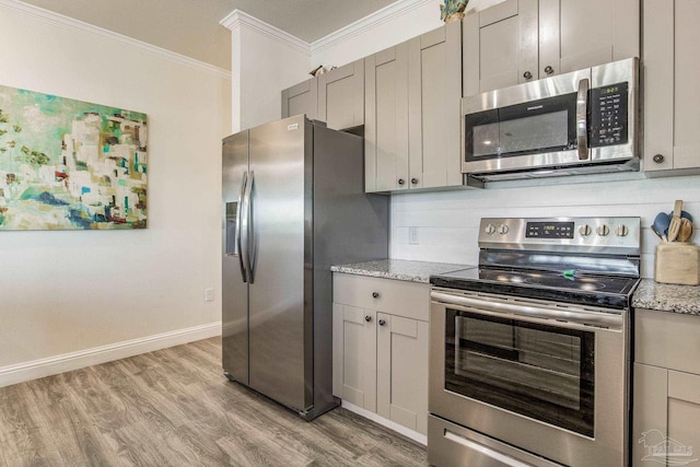 kitchen with appliances with stainless steel finishes, crown molding, light stone counters, and light hardwood / wood-style floors