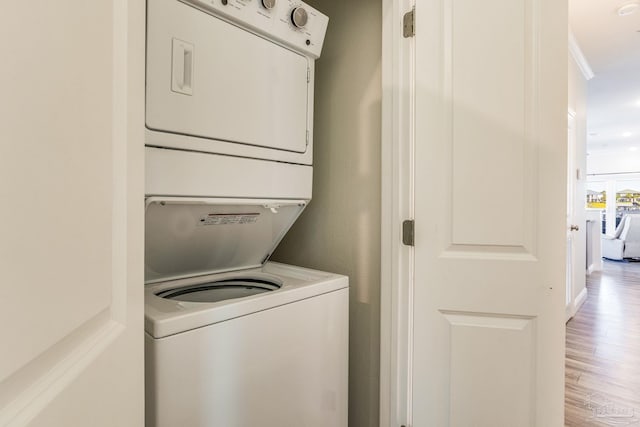 clothes washing area featuring stacked washer / drying machine, crown molding, and light hardwood / wood-style flooring