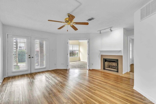 unfurnished living room featuring light wood-type flooring, a fireplace with flush hearth, a textured ceiling, visible vents, and a ceiling fan