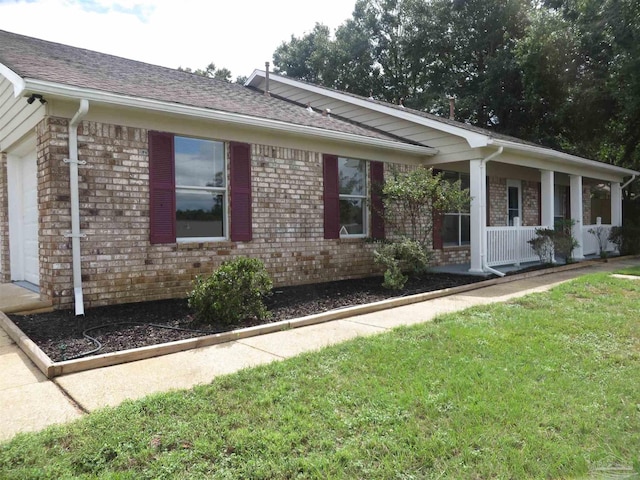 view of front of home with brick siding, a front yard, and covered porch