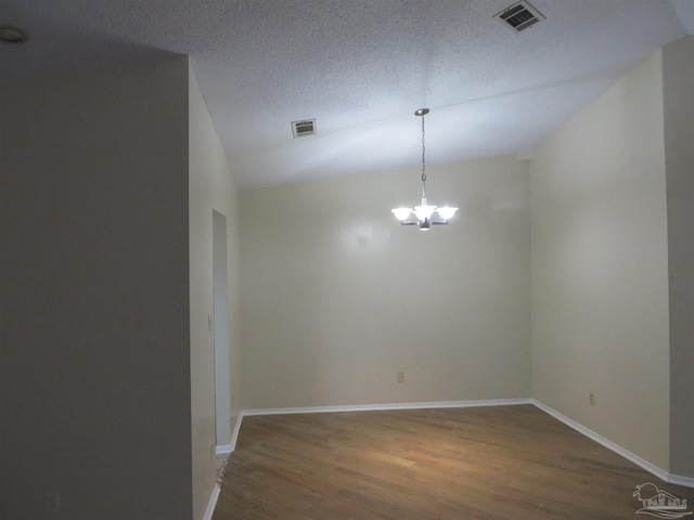 unfurnished room featuring an inviting chandelier, hardwood / wood-style flooring, vaulted ceiling, and a textured ceiling