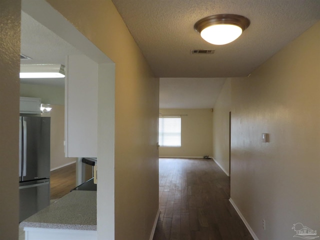 hall featuring dark wood-style flooring, visible vents, baseboards, and a textured ceiling