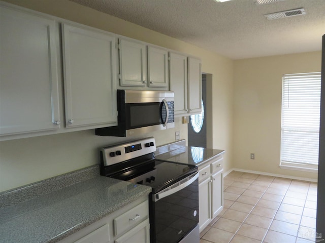 kitchen featuring visible vents, white cabinets, light tile patterned floors, a textured ceiling, and stainless steel appliances