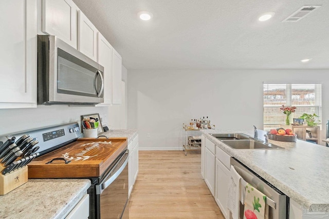 5252 Peach Dr, Pace, FL 32571 - kitchen with appliances with stainless steel finishes, a sink, light wood finished floors, white cabinets, and a textured ceiling