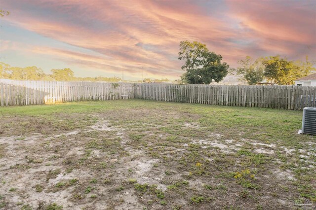 yard at dusk featuring a fenced backyard and central AC unit