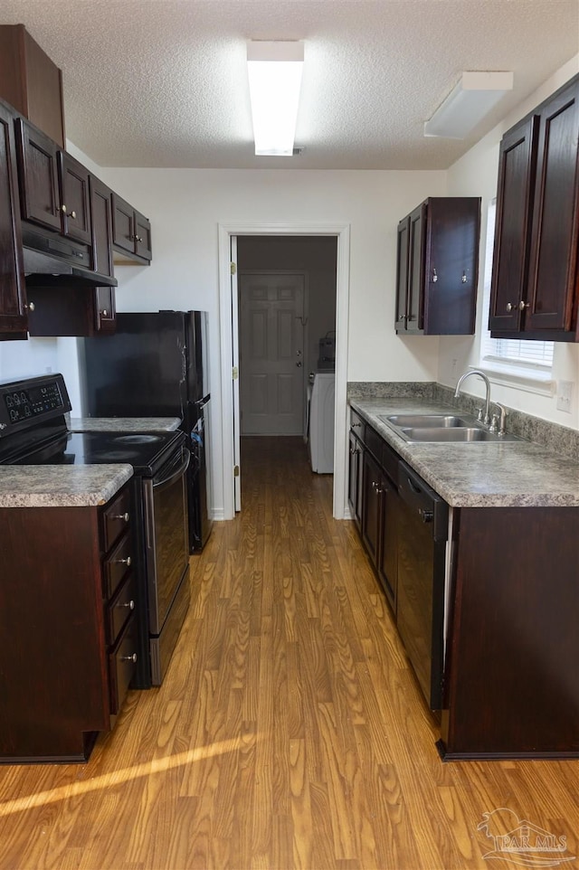 kitchen featuring dark brown cabinetry, under cabinet range hood, a sink, light wood finished floors, and black appliances