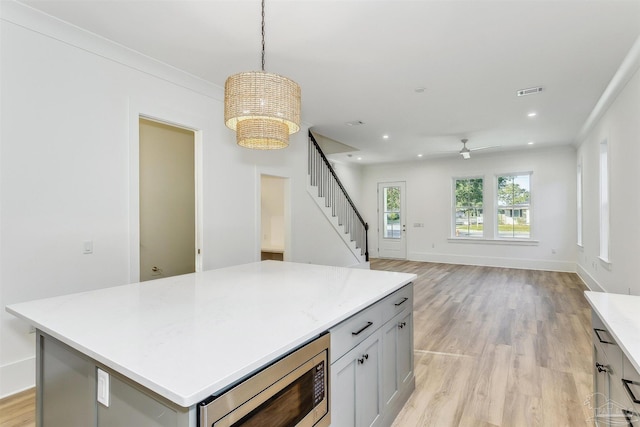 kitchen with light countertops, open floor plan, stainless steel microwave, and decorative light fixtures