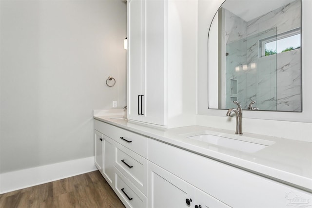 bathroom featuring double vanity, wood finished floors, a sink, and a marble finish shower