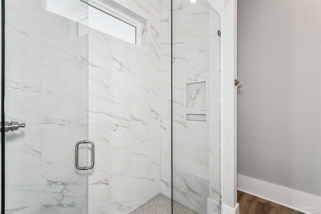 bathroom featuring a marble finish shower, baseboards, and wood finished floors