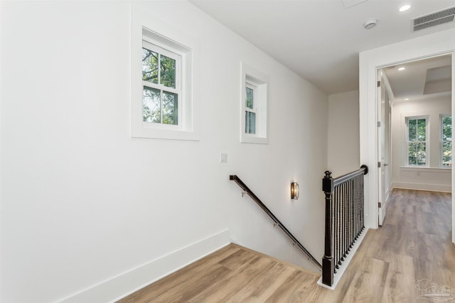 hallway featuring light wood-style flooring, visible vents, baseboards, and an upstairs landing