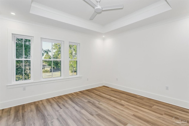 unfurnished room featuring light wood-style floors, a tray ceiling, ornamental molding, and baseboards