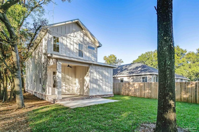 rear view of property with board and batten siding, a patio area, fence, and a lawn