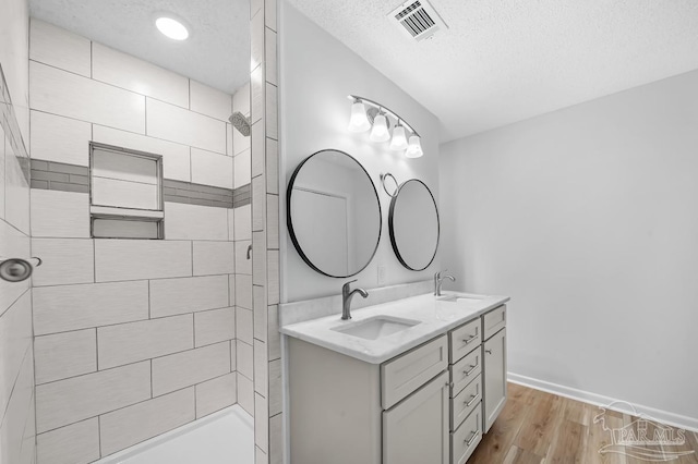 bathroom with wood-type flooring, a textured ceiling, a tile shower, and vanity