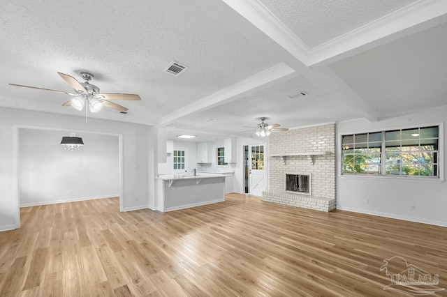 unfurnished living room with light wood-type flooring, a textured ceiling, beam ceiling, and a brick fireplace