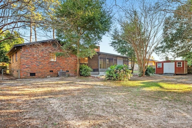 back of property with a sunroom, a storage shed, and central AC