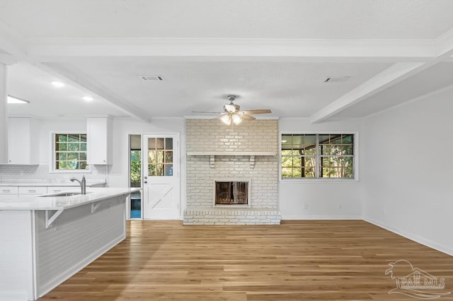 unfurnished living room with ceiling fan, sink, a brick fireplace, light hardwood / wood-style floors, and beamed ceiling