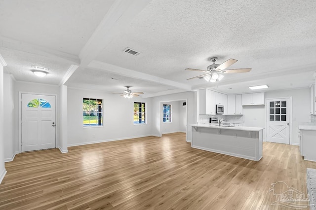 unfurnished living room with ceiling fan, sink, light wood-type flooring, beam ceiling, and a textured ceiling