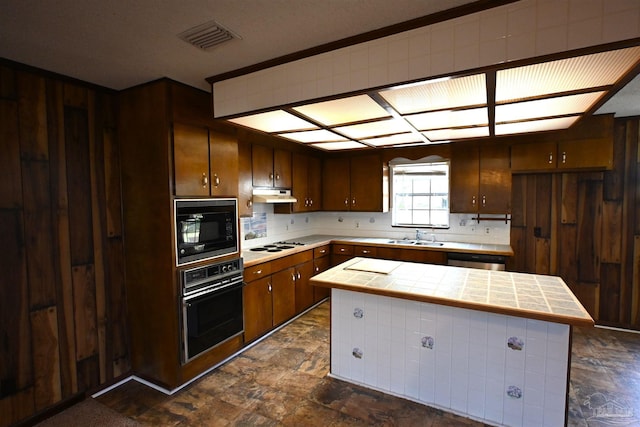 kitchen with sink, tile counters, a center island, and black appliances