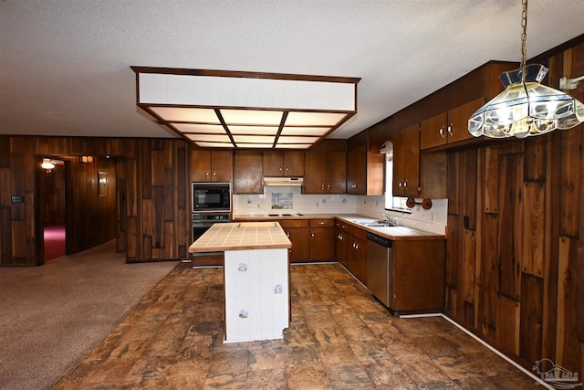 kitchen featuring pendant lighting, wood walls, black appliances, dark colored carpet, and sink