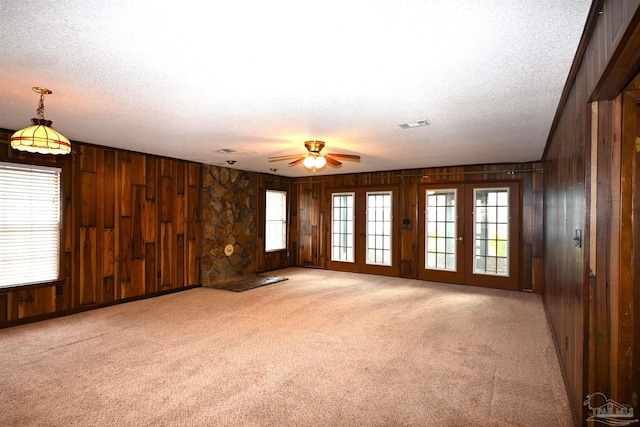 unfurnished room with a textured ceiling, ceiling fan, wooden walls, and carpet flooring