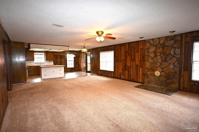 unfurnished living room with carpet, wood walls, ceiling fan, and a textured ceiling