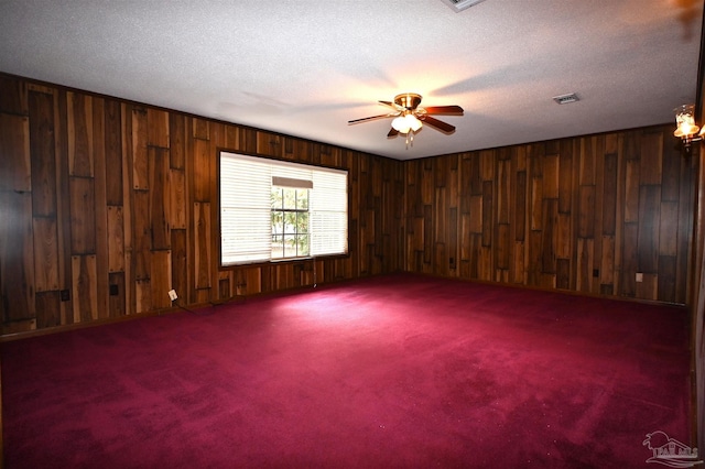 carpeted spare room featuring wooden walls, a textured ceiling, and ceiling fan