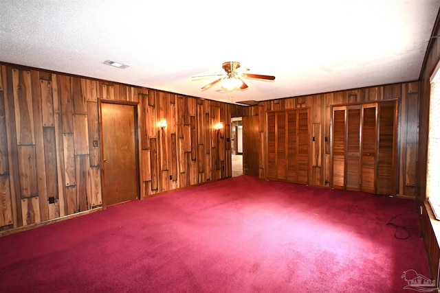 carpeted empty room with wood walls and ceiling fan