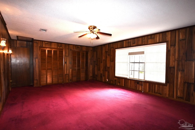 carpeted empty room featuring a textured ceiling, ceiling fan, and wooden walls