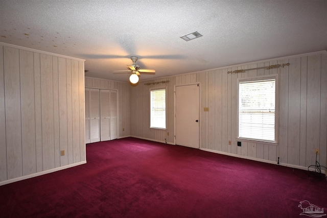 spare room with a textured ceiling, wooden walls, carpet floors, ceiling fan, and ornamental molding