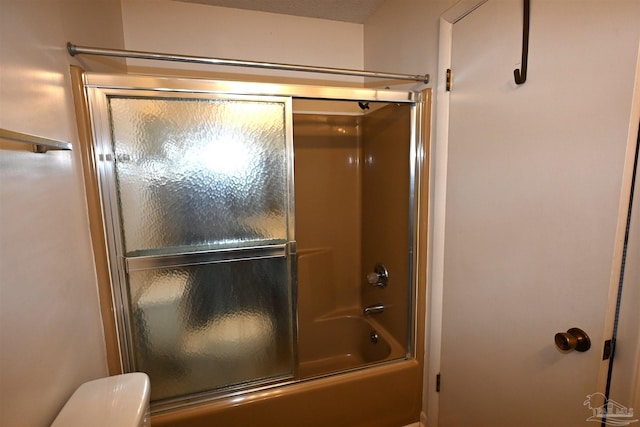 bathroom featuring combined bath / shower with glass door and toilet