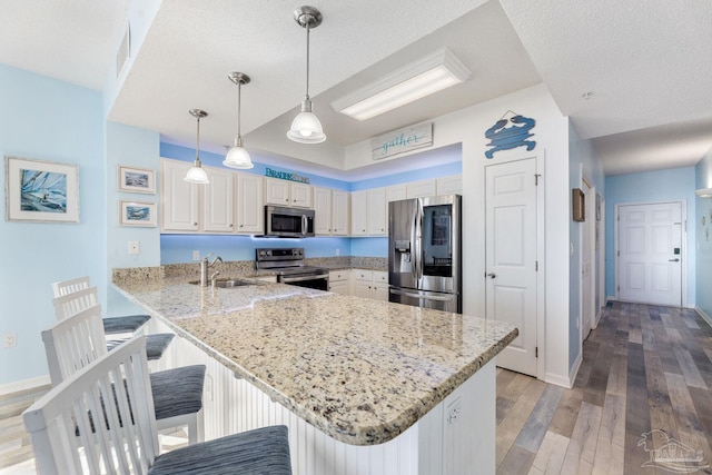 kitchen with sink, a breakfast bar area, appliances with stainless steel finishes, decorative light fixtures, and kitchen peninsula