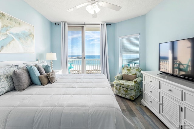 bedroom with multiple windows, access to exterior, ceiling fan, dark wood-type flooring, and a textured ceiling