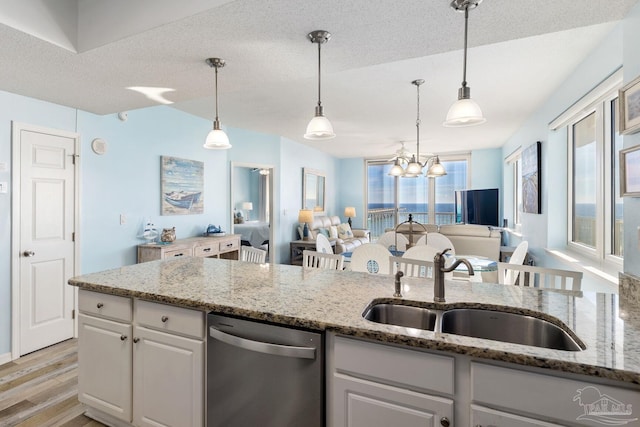 kitchen with sink, hanging light fixtures, stainless steel dishwasher, light stone countertops, and white cabinets