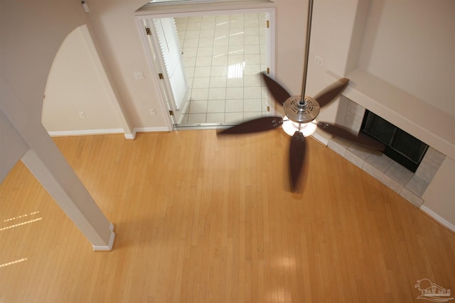 room details featuring ceiling fan, a tiled fireplace, baseboards, and wood finished floors