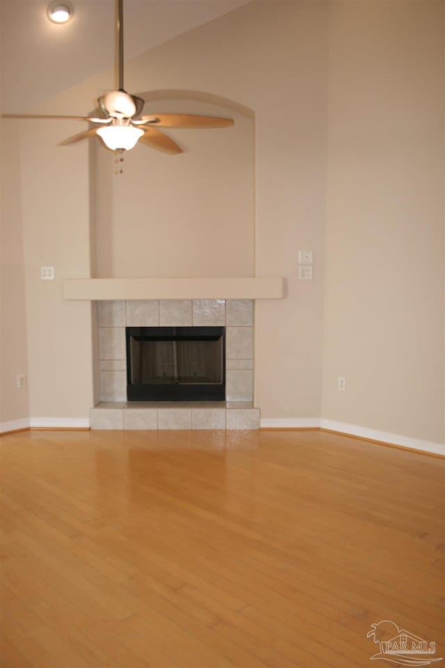 unfurnished living room featuring ceiling fan, wood finished floors, a tile fireplace, and lofted ceiling