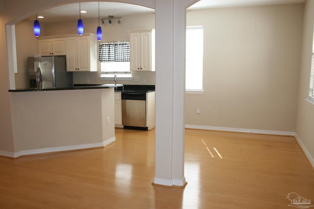 kitchen with arched walkways, light wood-style floors, white cabinets, appliances with stainless steel finishes, and dark countertops