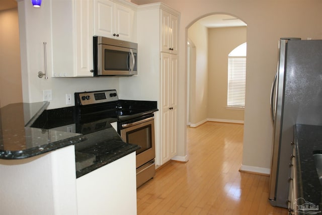 kitchen featuring arched walkways, white cabinets, dark stone countertops, stainless steel appliances, and light wood-type flooring