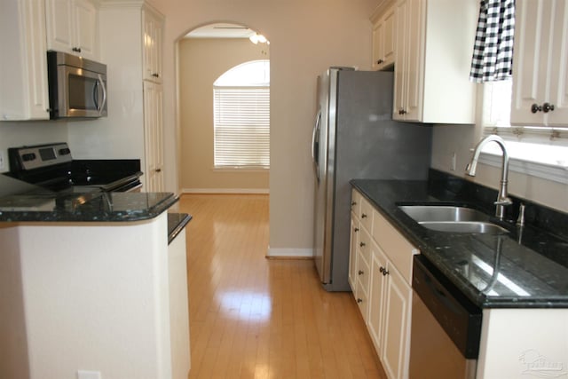 kitchen featuring light wood-type flooring, appliances with stainless steel finishes, dark stone counters, and a sink