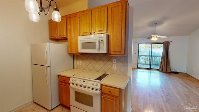 kitchen featuring tasteful backsplash, decorative light fixtures, light wood-type flooring, white appliances, and ceiling fan with notable chandelier