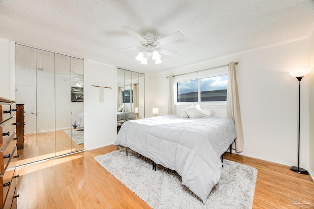 bedroom with ceiling fan, ornamental molding, a textured ceiling, light hardwood / wood-style floors, and multiple closets