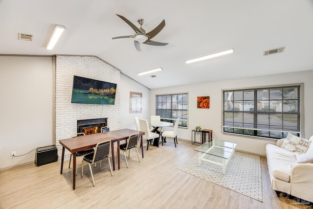 living room featuring a fireplace, light wood-type flooring, vaulted ceiling, and ceiling fan